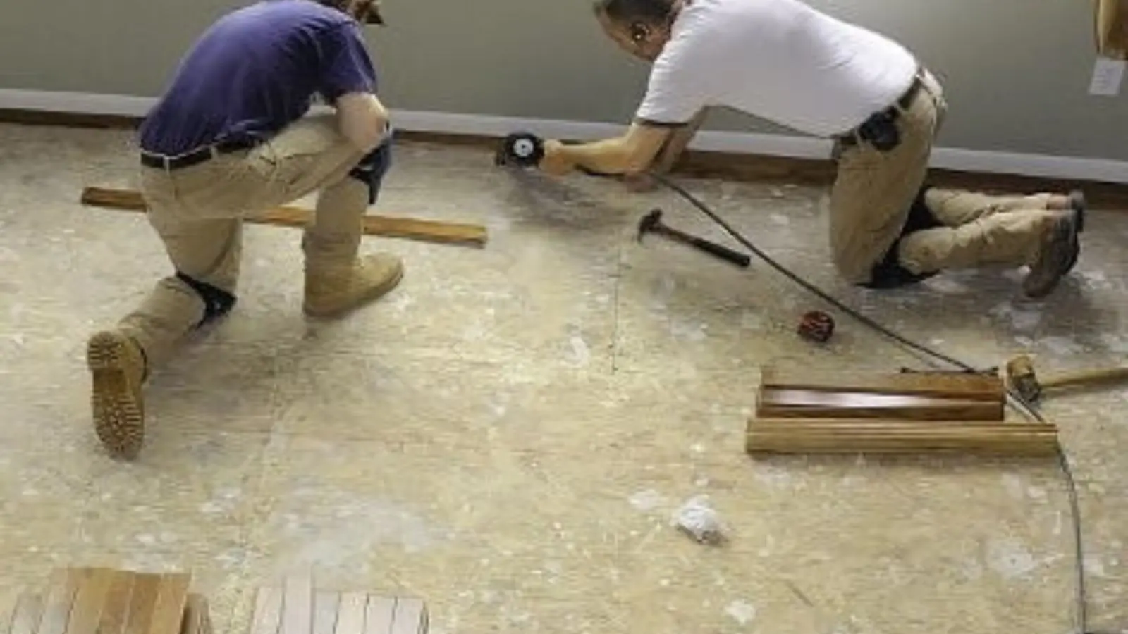 Two workers kneeling on a bare subfloor during water damage repair